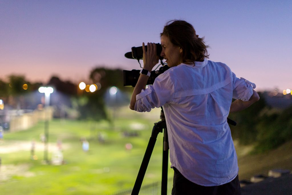 portrait of the artist looking through a camera lens on a tripod