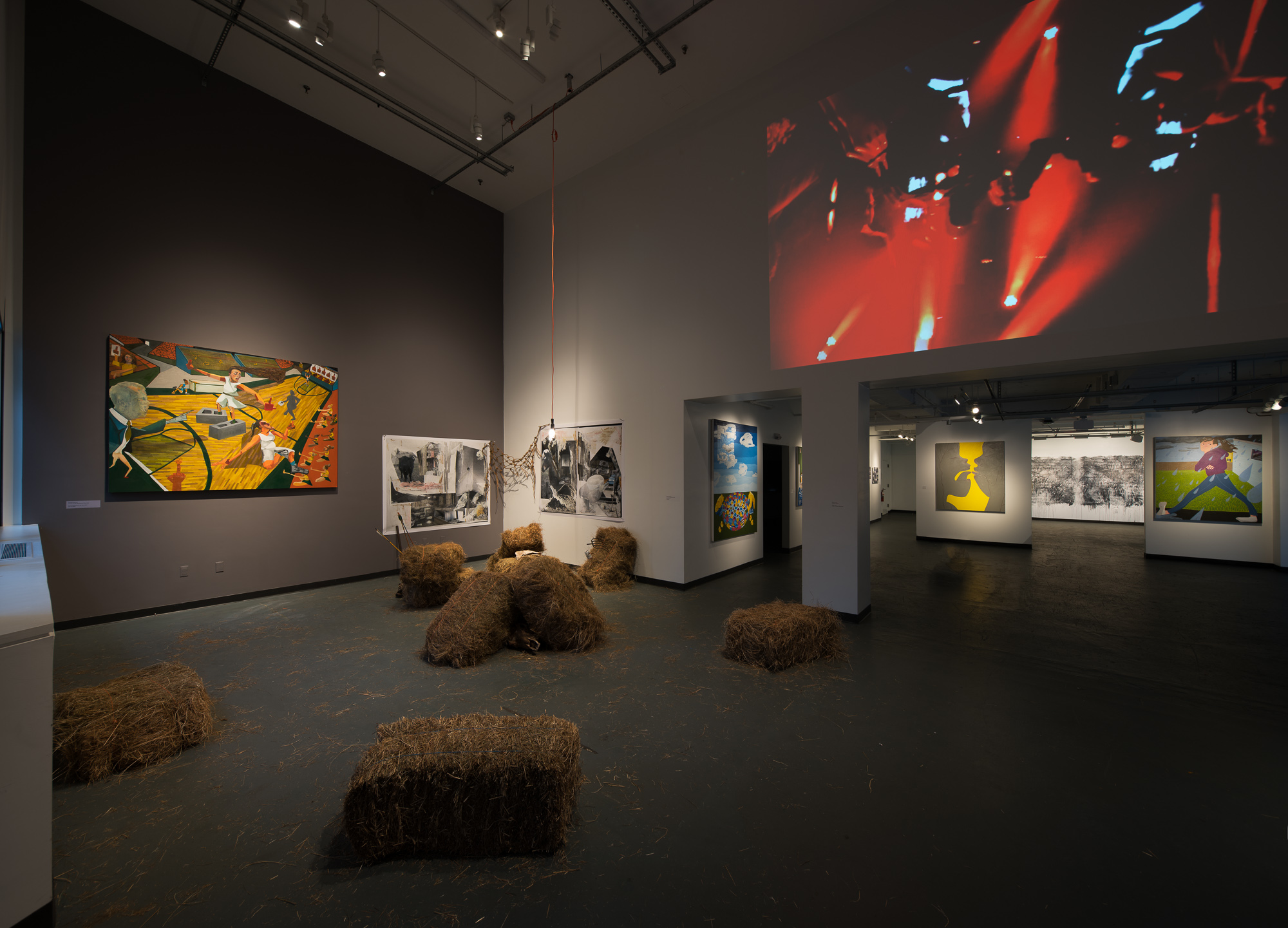 dissonance exhibit featuring paintings and projections on walls, hay bales on floor