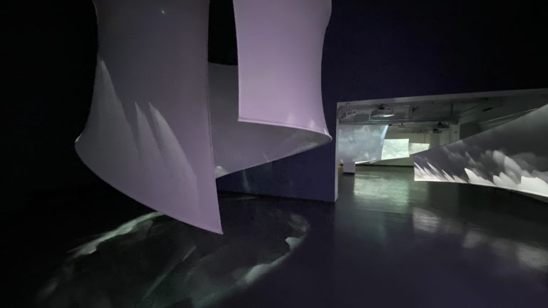 A series of white sheets installed in a darkly lit room.