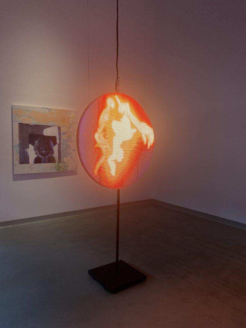 A circular LED stand in a room displaying an abstract orange fire.