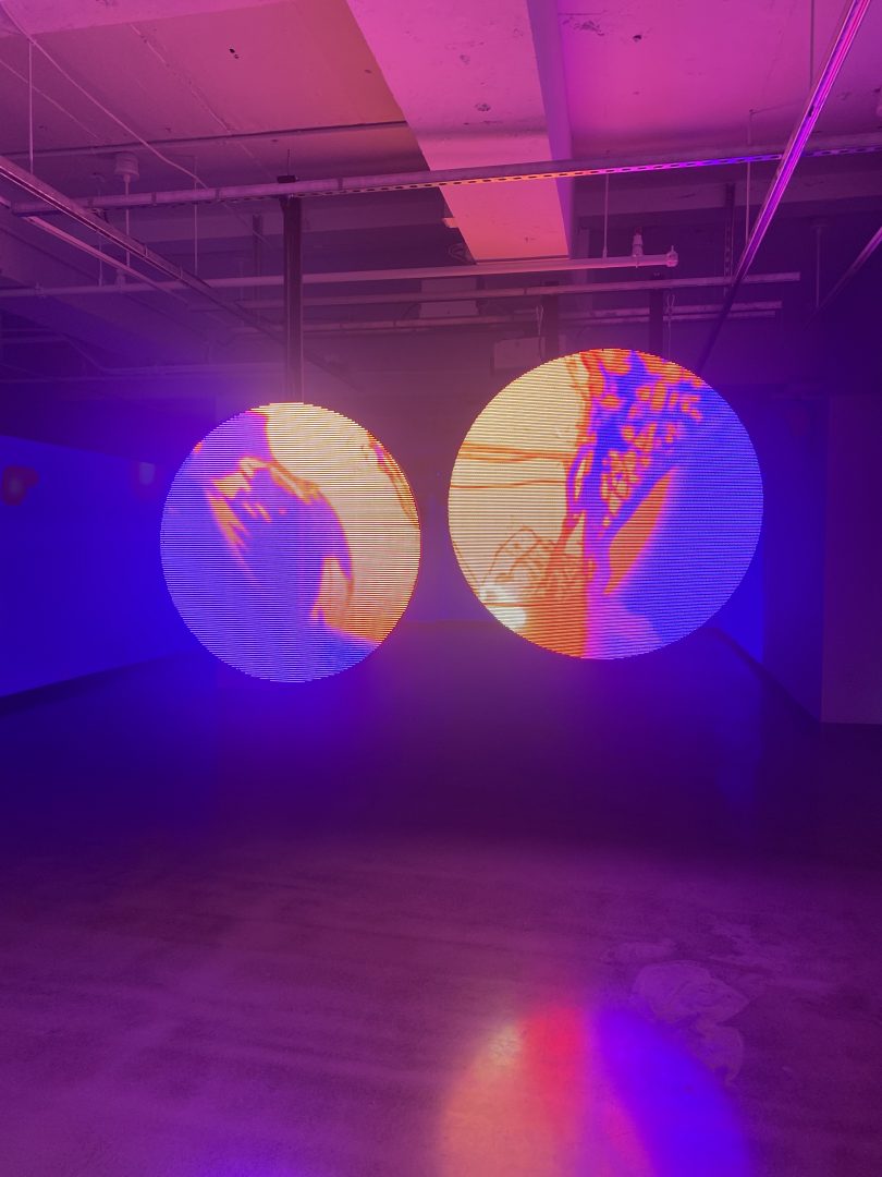 Two circular LED stands in a room displaying an abstract orange visuals.