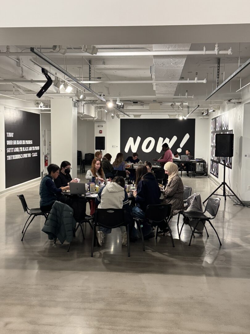 Students sit around a table making zines together in an art gallery.