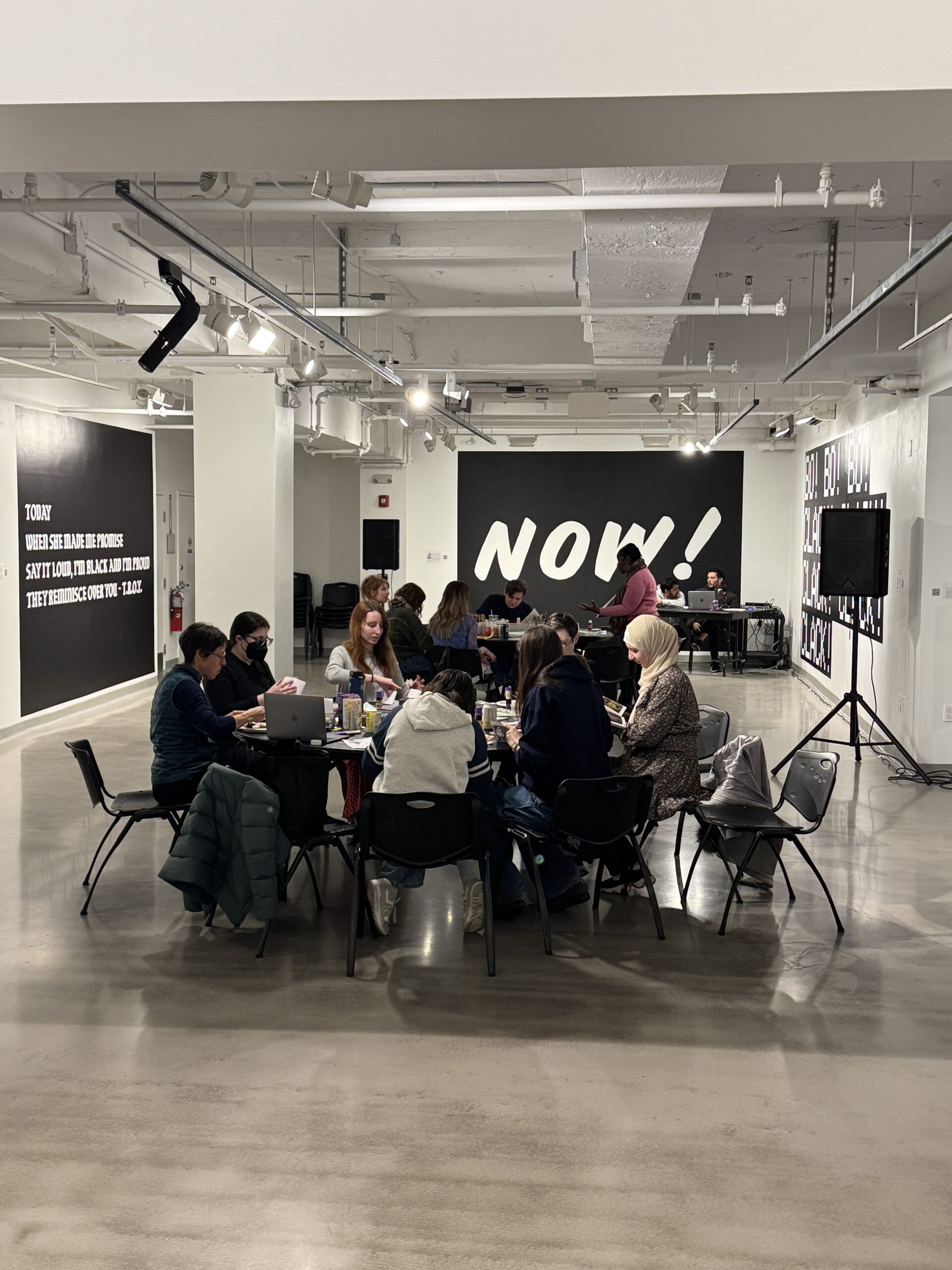 Students sit around a table making zines together in an art gallery.